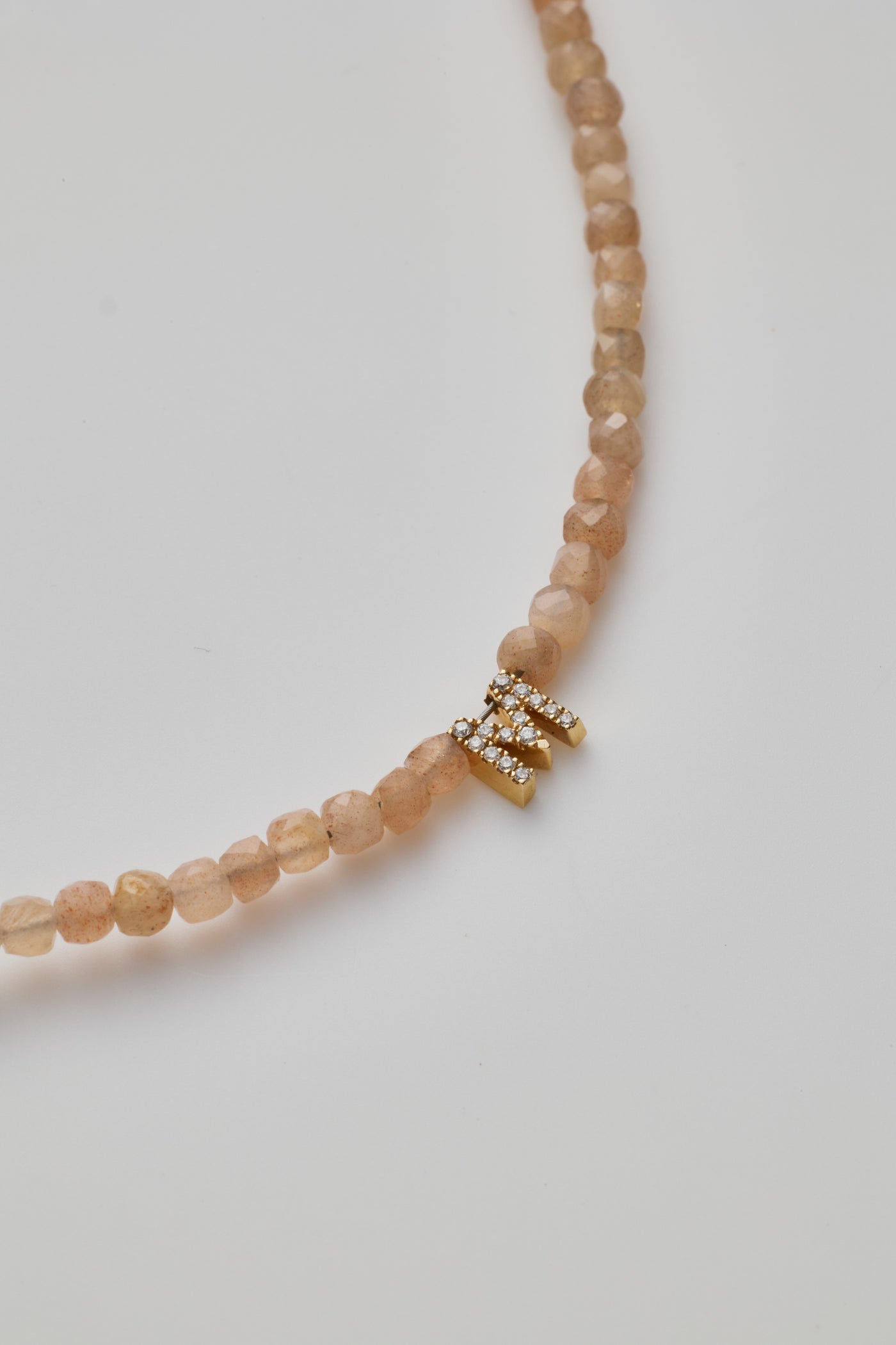 Delicate bracelet with blush-coloured moonstone beads and a diamond alphabet charm, elegantly crafted.