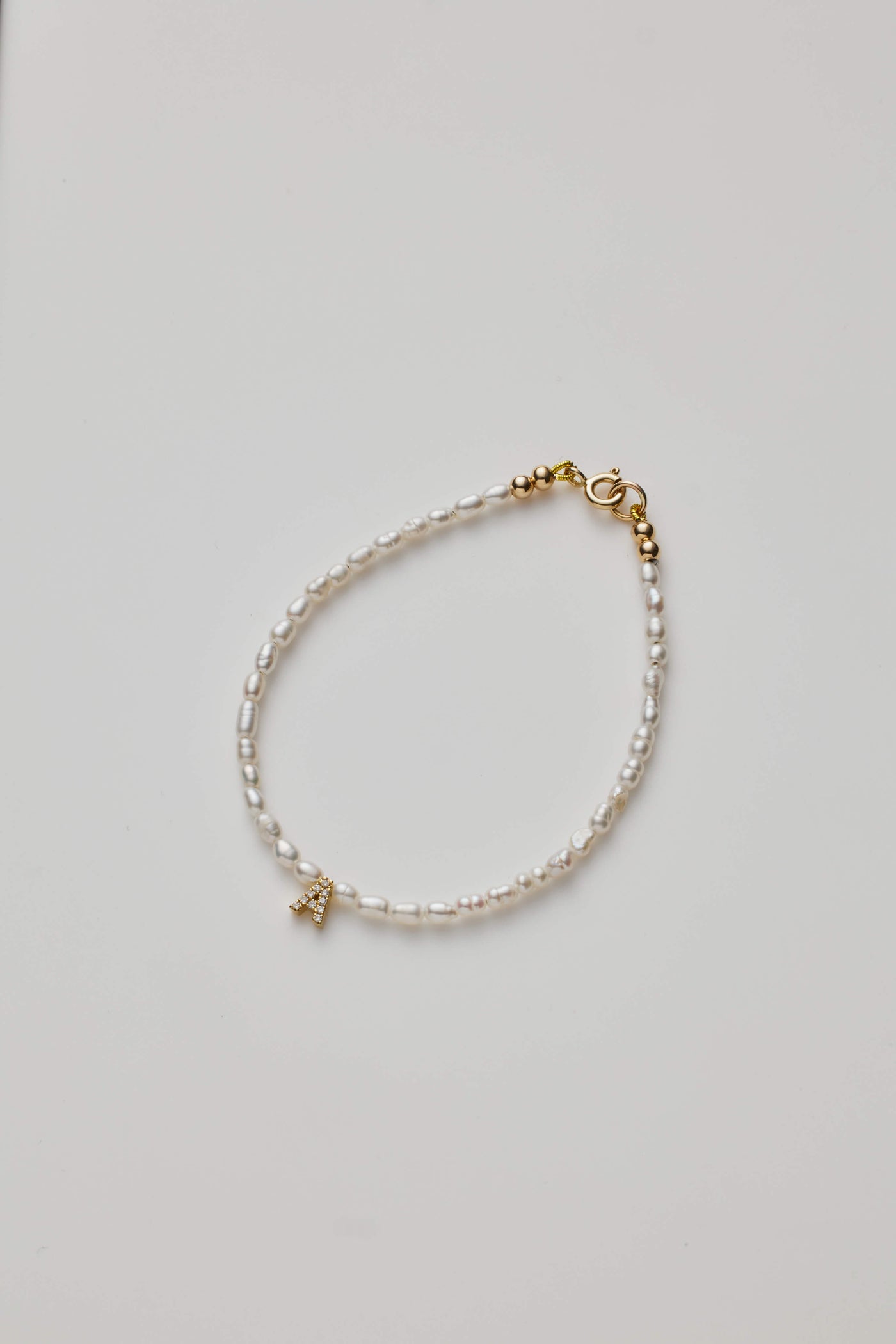 Delicate bracelet with small pearls and a diamond alphabet A charm on grey background