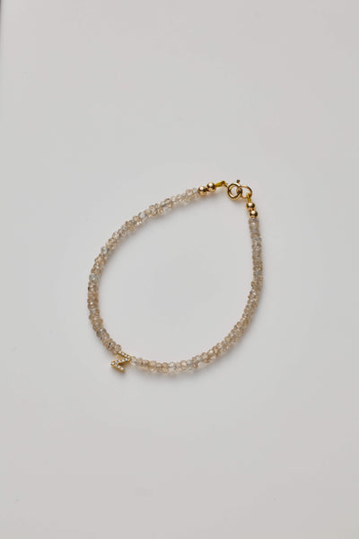 Delicate bracelet with natural zircon beads and a diamond alphabet charm, elegantly crafted.