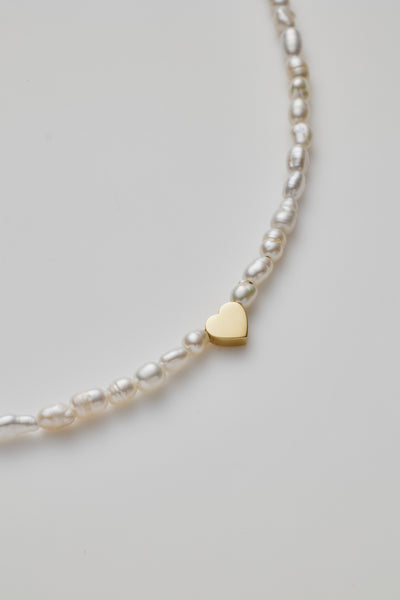 Delicate bracelet with lustrous pearls and a gold heart charm, elegantly crafted.