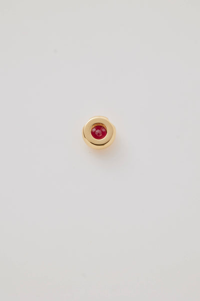 The reverse side view of a July Birthstone Charm featuring a vibrant ruby gemstone in a polished gold setting. Photographed on a pale grey background. 