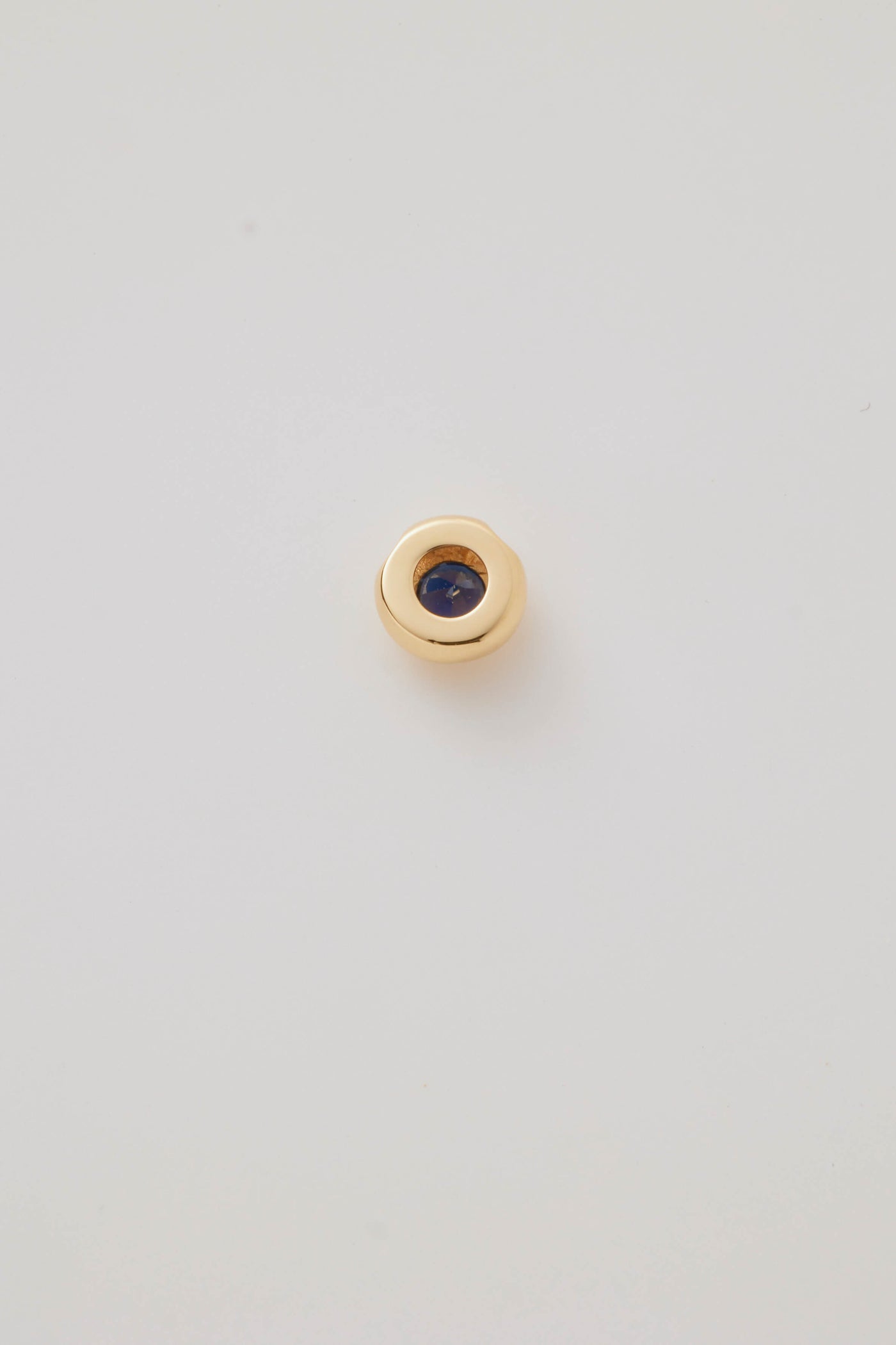 The reverse side view of the September Birthstone Charm featuring a deep blue sapphire gemstone in an elegant gold setting. Photographed on a light grey background.