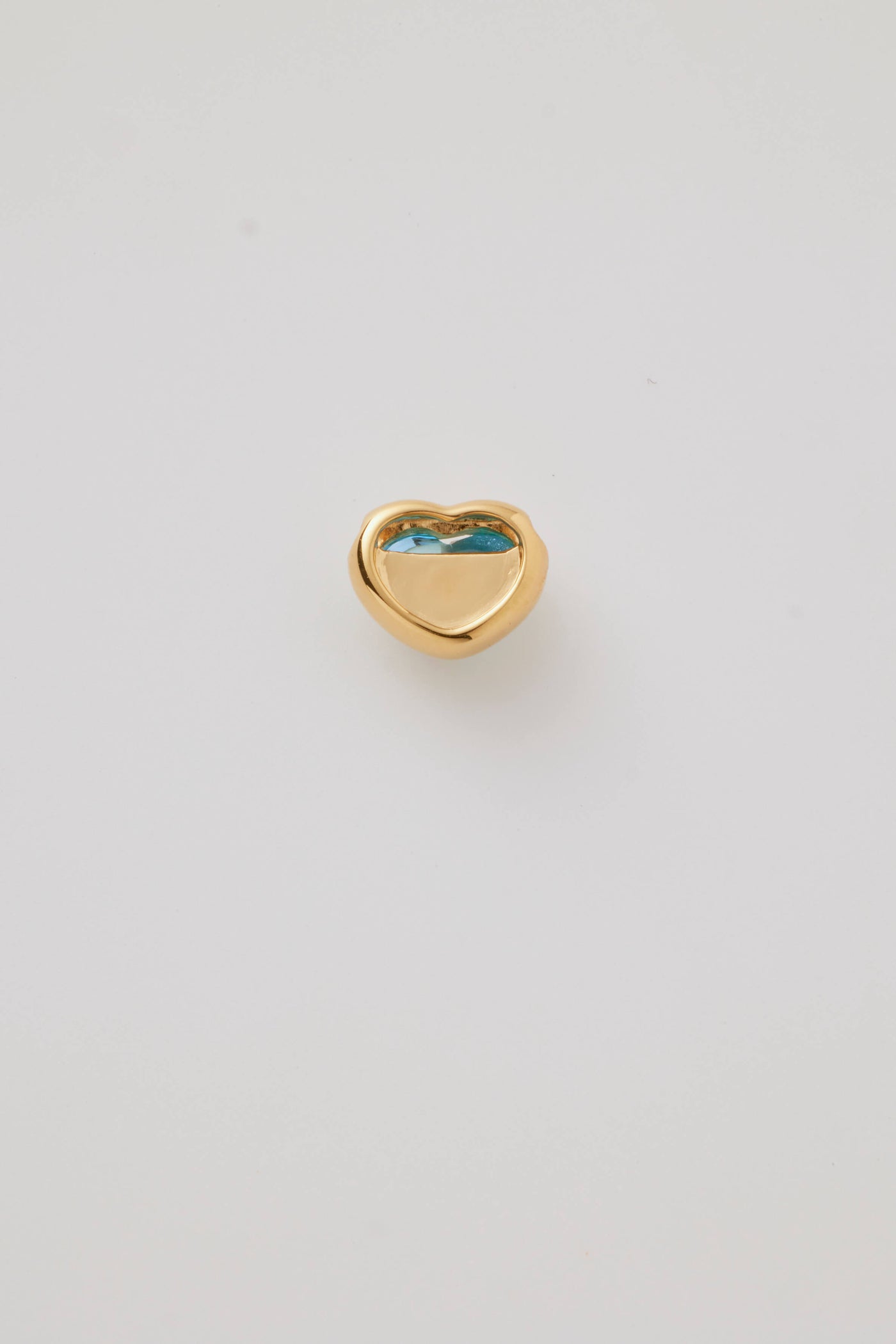 The reverse side shows the back of a blue topaz cabochon stone set in a polished gold heart frame, displayed on a light grey background. Elegant and timeless.