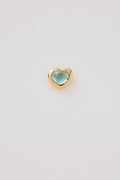 A blue topaz cabochon stone set in a polished gold heart frame, displayed on a light grey background. Elegant and timeless.