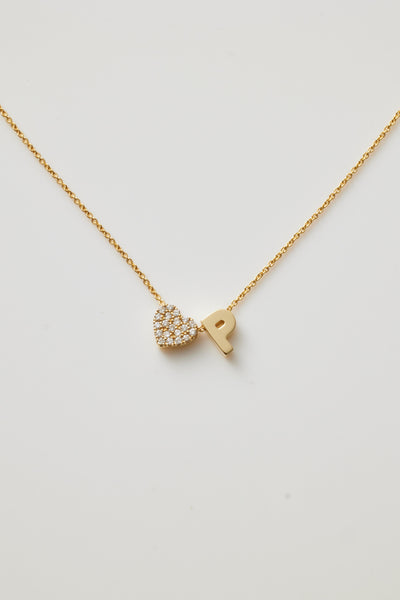 A gold necklace featuring a delicate chain with two charms: a sparkling, diamond-studded heart and a bold gold letter "P," positioned side by side.