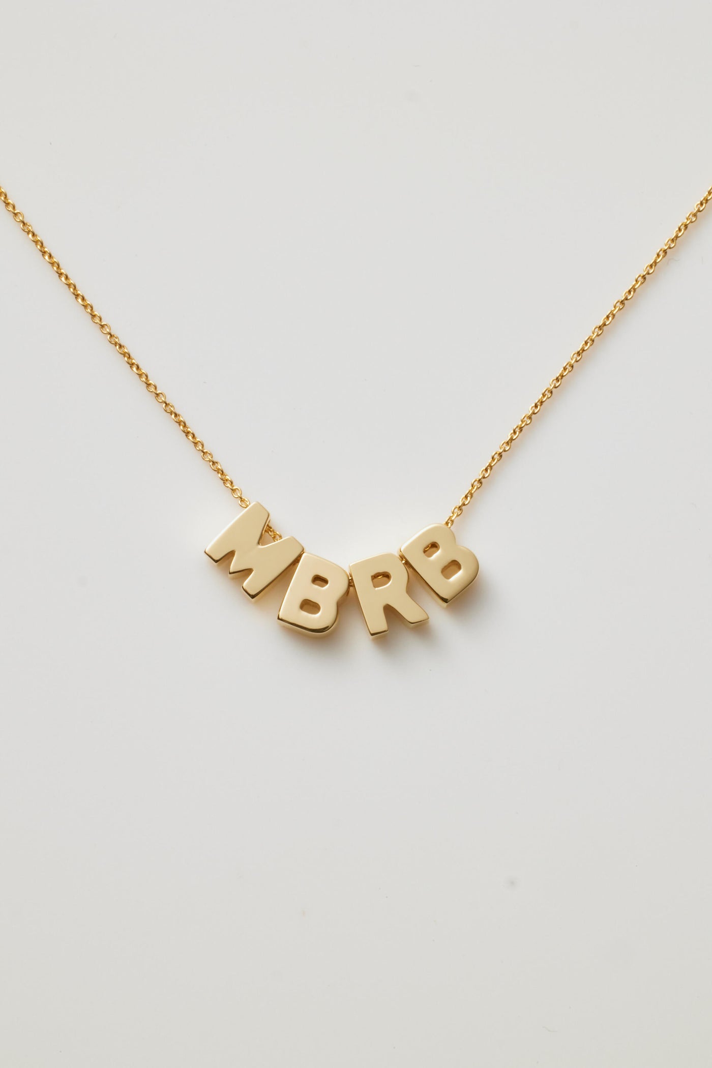 A delicate 18k solid gold necklace named the Four Letters Necklace in 18k Gold showcases a fine chain with letters MBRB letter charm pendants, elegantly displayed against a plain white background.