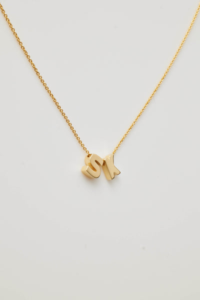 The Two Letters Necklace in 18k Gold showcases a delicate 18k solid gold chain with two gold letter charms, "S" and "K," elegantly positioned close together at the centre, all set against a plain white background.