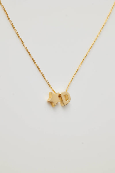 The One Letter and Star Necklace in 18k Gold features a delicate gold chain with two charms: a capital letter 'D' and a small star. Both charms, crafted from 18k solid gold, hang elegantly close together in the centre against a plain white background, highlighting the necklace's refined beauty.