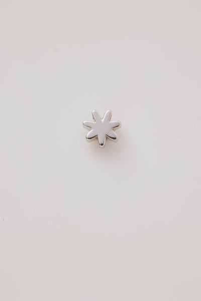 The reverse side of a white gold daisy charm, softly lit on a light grey background.