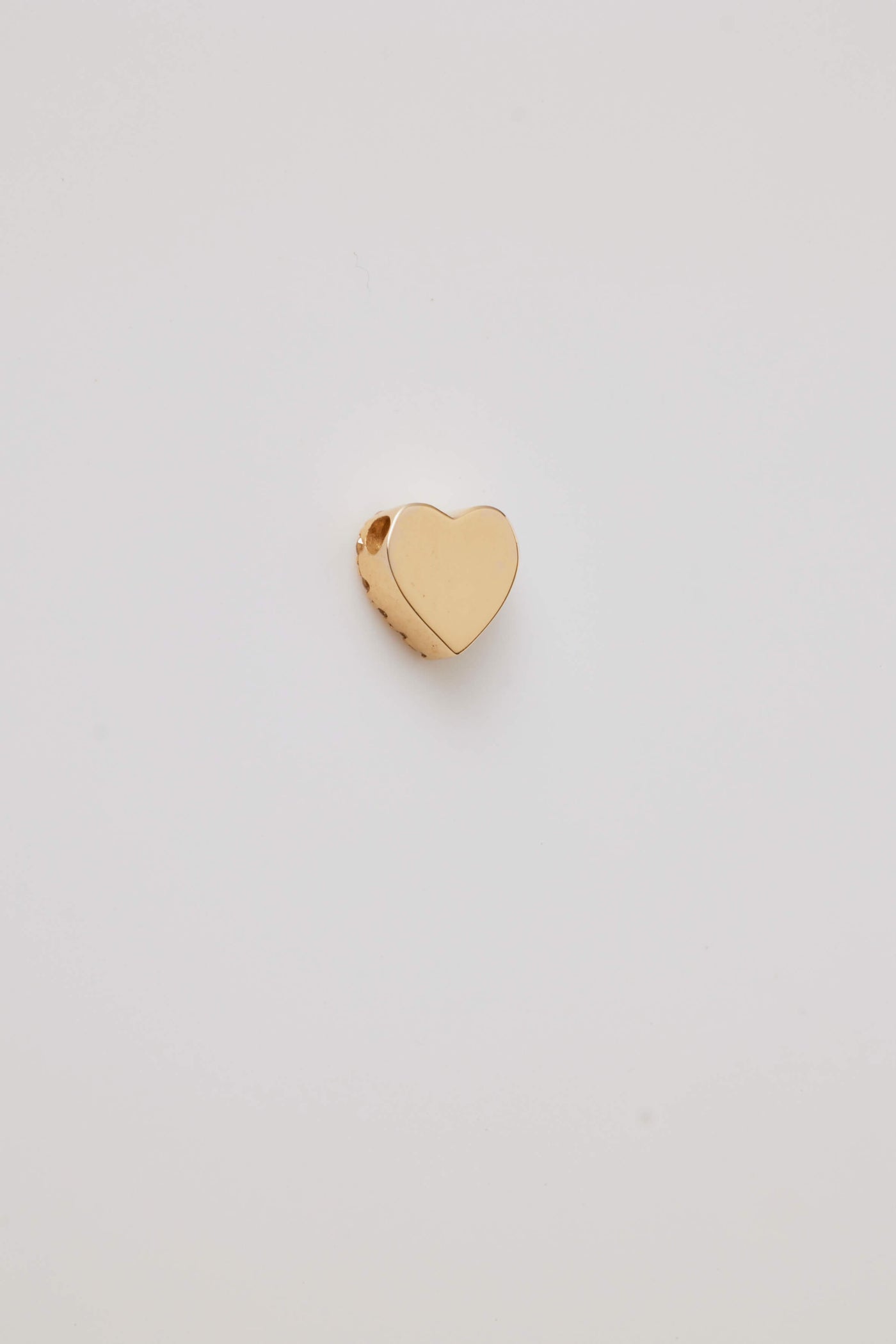 The reverse side of a solid gold miniature heart charm, is elegantly adorned with vibrant pink sapphire gemstones. The tiny heart-shaped design is pavé-set with sparkling pink sapphires, creating a vivid, eye-catching effect. A small hole at the top allows the charm to be easily threaded through to a gold chain adding a touch of luxury and romance.