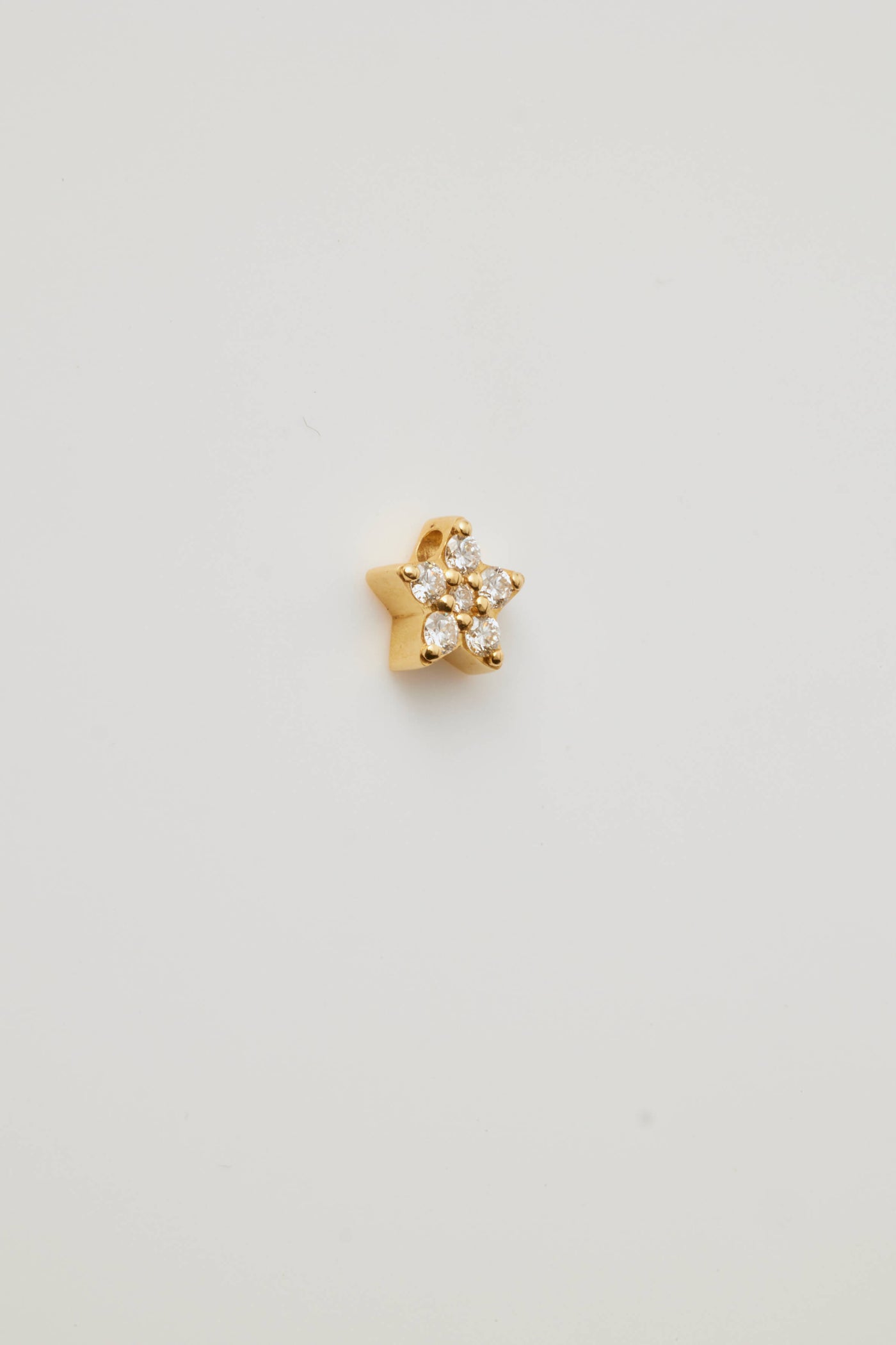 A side view showing a solid gold star charm adorned with sparkling diamonds. The five-pointed star charm features brilliant-cut diamonds, creating a shimmering effect. A small hole at the top of the allows the charm to be threaded through with a necklace chain.