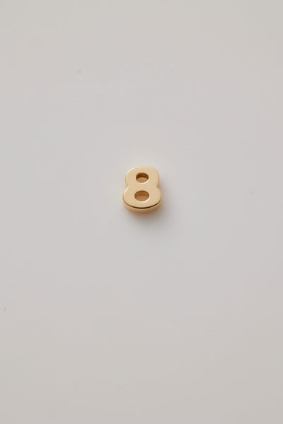 Three-dimensional number charms, each representing a number from 0 to 9, crafted from 18-karat solid gold. Each charm has a sleek, polished surface that radiates a rich, golden glow, adding a touch of luxury. A small hole is integrated at the top of each charm for easy attachment to a chain or bracelet. 