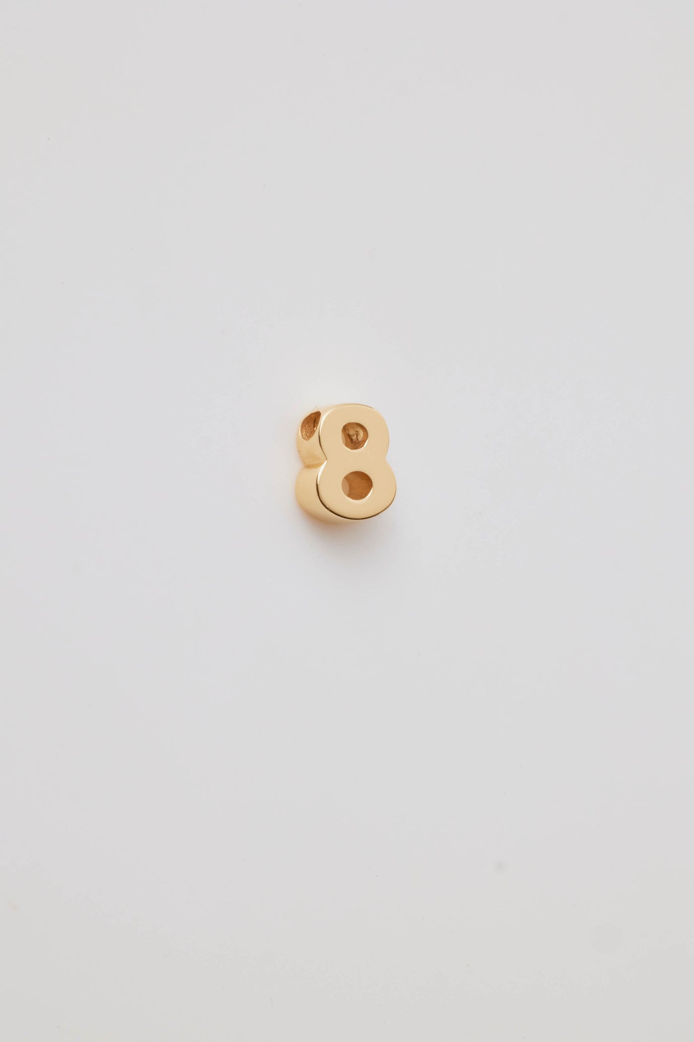 Three-dimensional number charms, each representing a number from 0 to 9, crafted from 18-karat solid gold. Each charm has a sleek, polished surface that radiates a rich, golden glow, adding a touch of luxury. A small hole is integrated at the top of each charm for easy attachment to a chain or bracelet. 