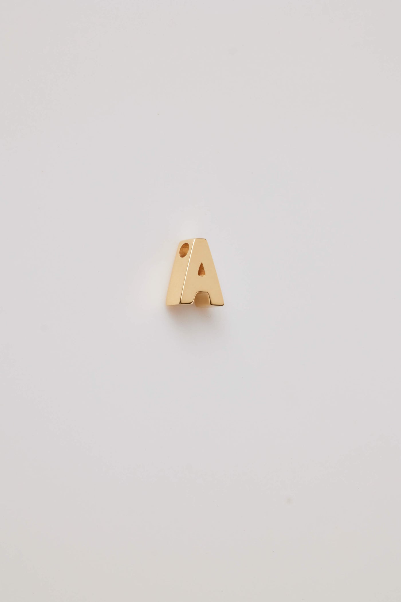 A three-dimensional charm crafted from 18-karat gold, shaped into a bold and elegant letter from the alphabet. The charm has a smooth, polished surface that gleams under light, highlighting its luxurious golden hue. Its edges are slightly rounded for a refined and sophisticated finish. The charm features a small, discreet hole at the top, allowing it to be easily threaded on to a necklace chain or bracelet. The overall design is both modern and timeless, exuding a sense of opulence and personalisation.