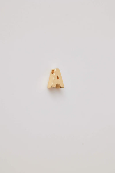 A three-dimensional charm crafted from 18-karat gold, shaped into a bold and elegant letter from the alphabet. The charm has a smooth, polished surface that gleams under light, highlighting its luxurious golden hue. Its edges are slightly rounded for a refined and sophisticated finish. The charm features a small, discreet hole at the top, allowing it to be easily threaded on to a necklace chain or bracelet. The overall design is both modern and timeless, exuding a sense of opulence and personalisation.