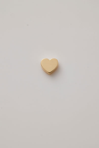 A beautifully crafted gold heart charm made from polished 18-karat gold. The charm features a classic heart shape with a sleek, smooth finish and a precise hole through the centre, designed for threading a gold chain. 