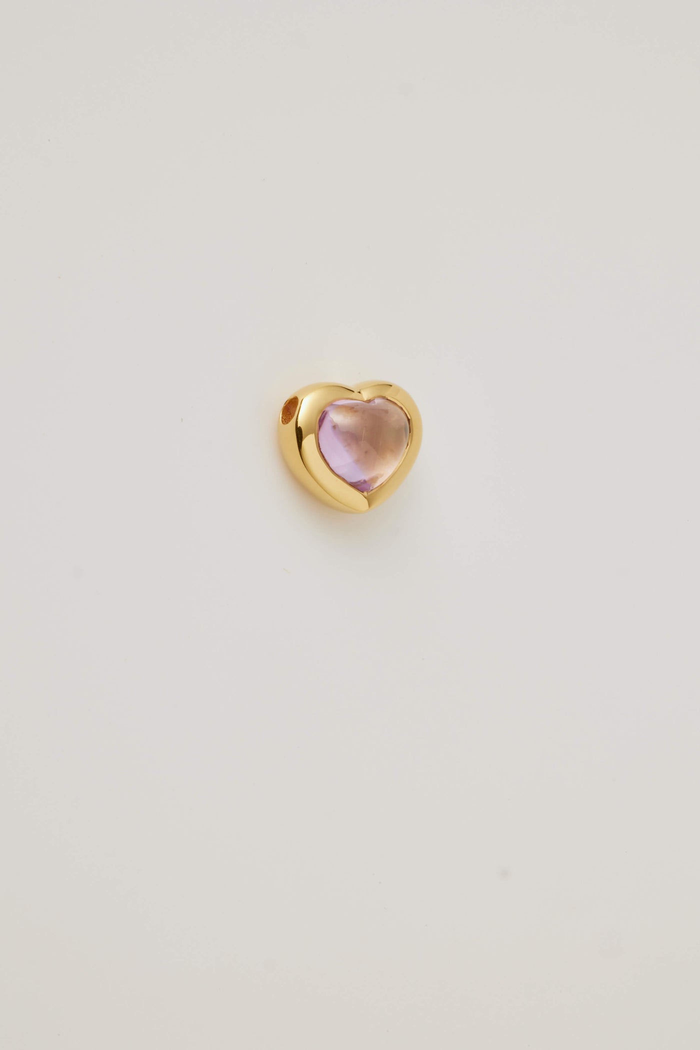 The side profile of a pink topaz cabochon stone set in a polished gold heart frame, is displayed on a light grey background. Elegant and timeless.