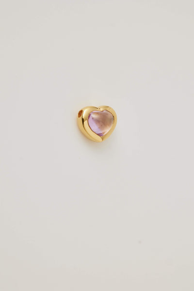 The side profile of a pink topaz cabochon stone set in a polished gold heart frame, is displayed on a light grey background. Elegant and timeless.