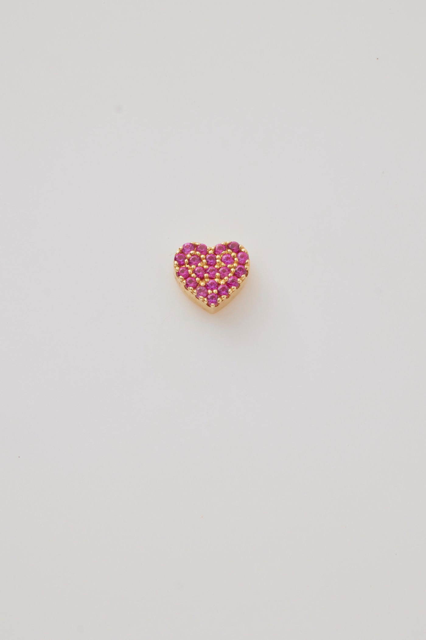 A solid gold miniature heart charm set with deep red ruby gemstones. The heart-shaped charm has a highly polished surface pavé-set in brilliant, vibrant rubies that add a touch of richness and elegance. A small gold hole at the top provides an easy attachment point for a chain or bracelet, making it a perfect accessory for a delicate and luxurious look.