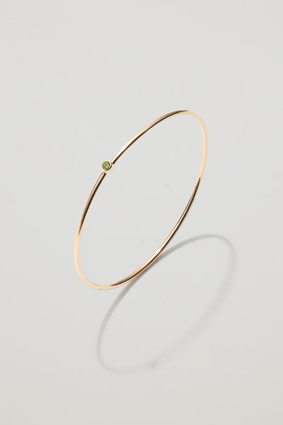 Solid gold bangle with an August peridot birthstone, symbolising optimism and renewal.