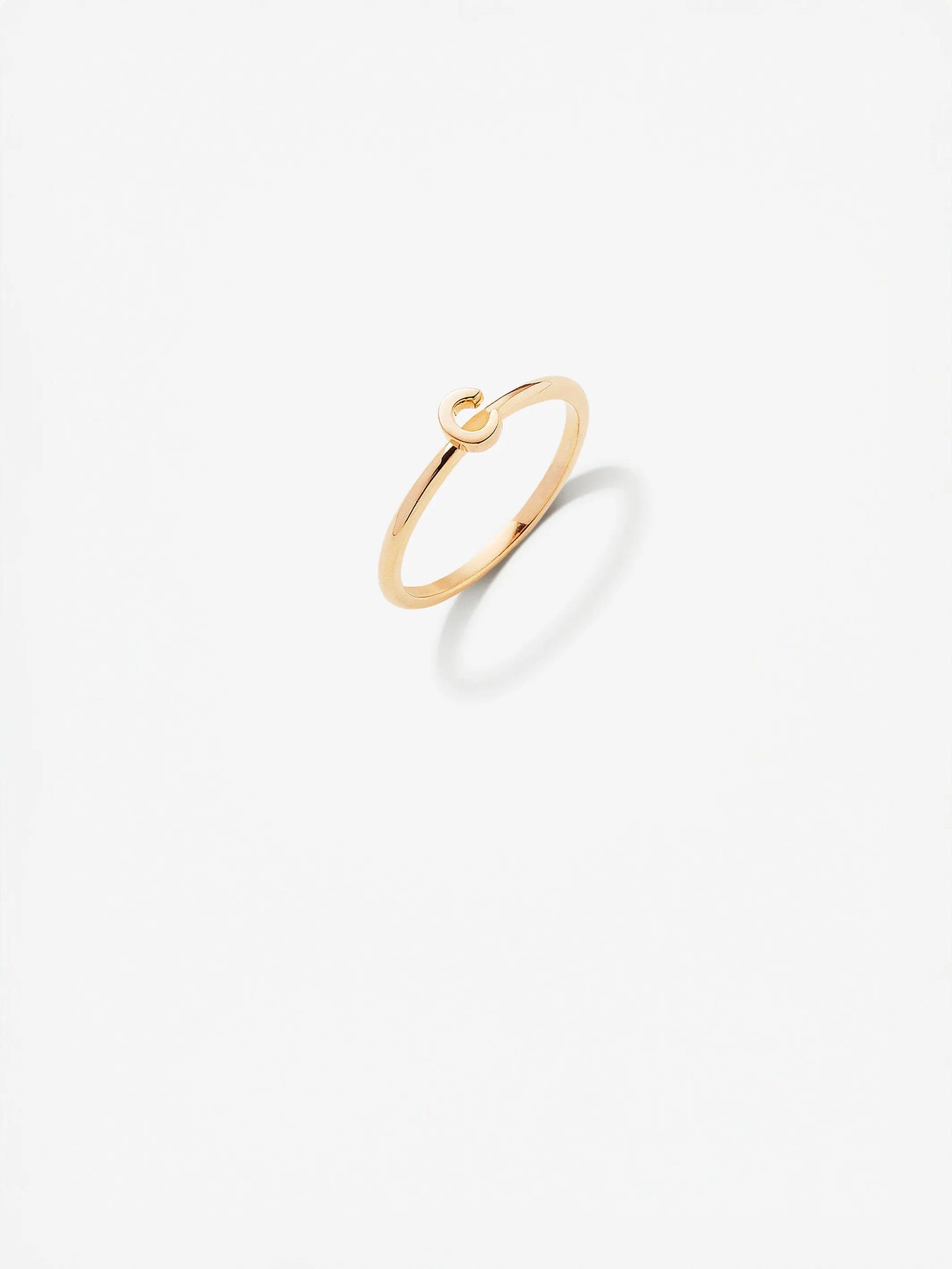 The Letter C Ring in 18k gold is a minimalist piece featuring a small, elegant loop on top. Set against a white background, the ring's faint shadow accentuates its sleek and delicate design. Custom sizes are available to ensure the perfect fit for this exquisite piece.