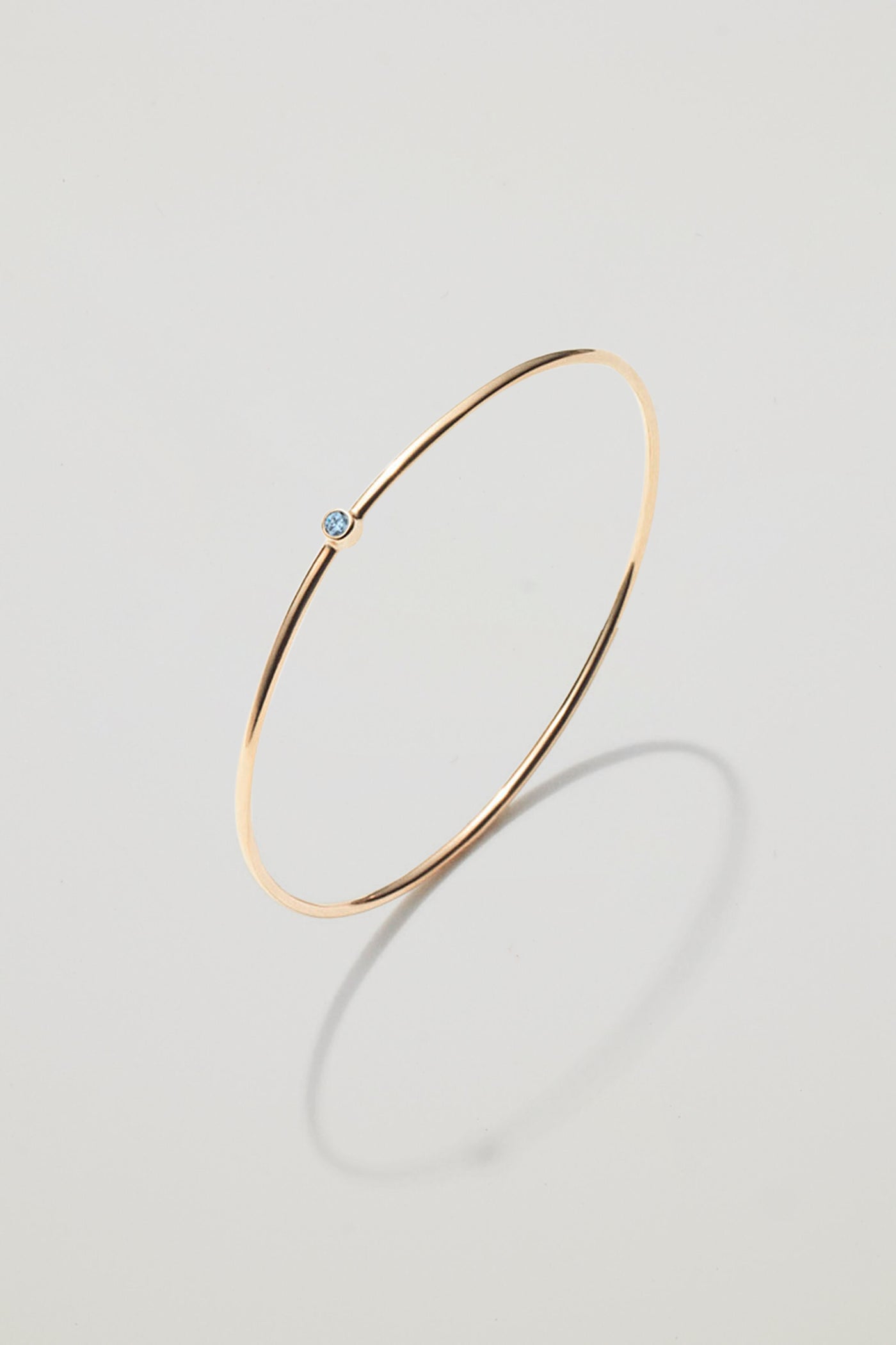 Solid gold bangle with a March aquamarine birthstone, symbolising renewal and courage.