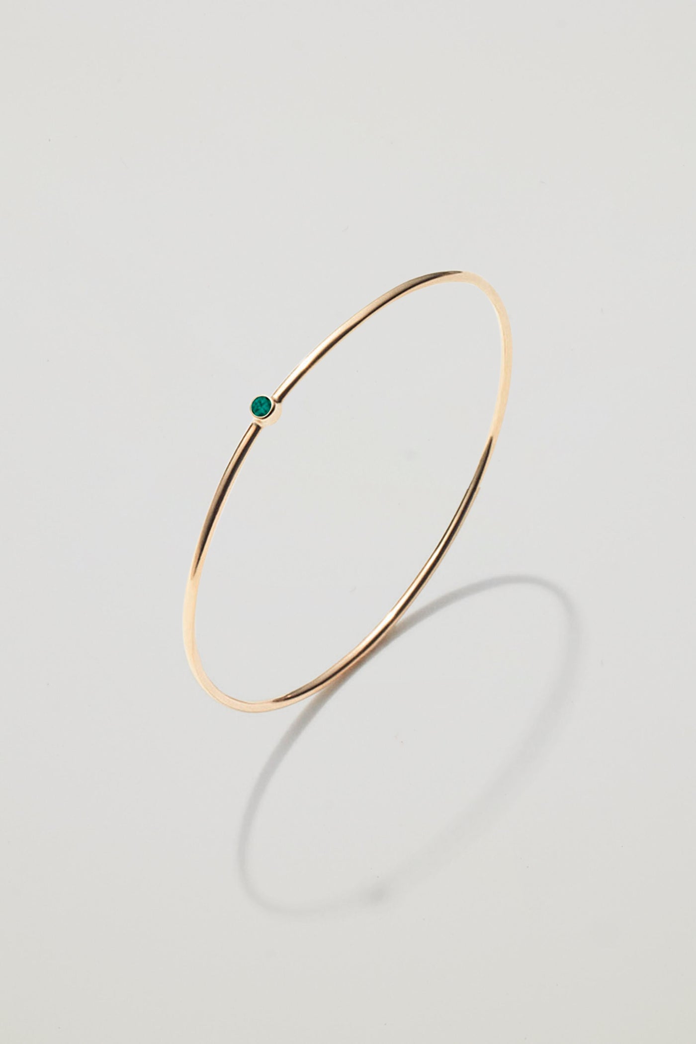 Solid gold bangle with a May emerald birthstone, symbolising growth and harmony.