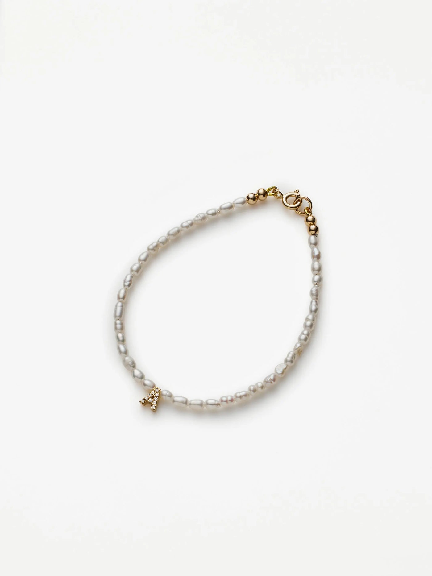 Presenting the One Letter Bracelet in Diamonds, Pearl, and 18k Gold: a delicate bracelet showcasing an array of white, rectangular beads and a small Eiffel Tower charm. It is adorned with luxurious 18k solid gold accents and securely fastened with a gold clasp. The background features a plain white setting to highlight its elegance.