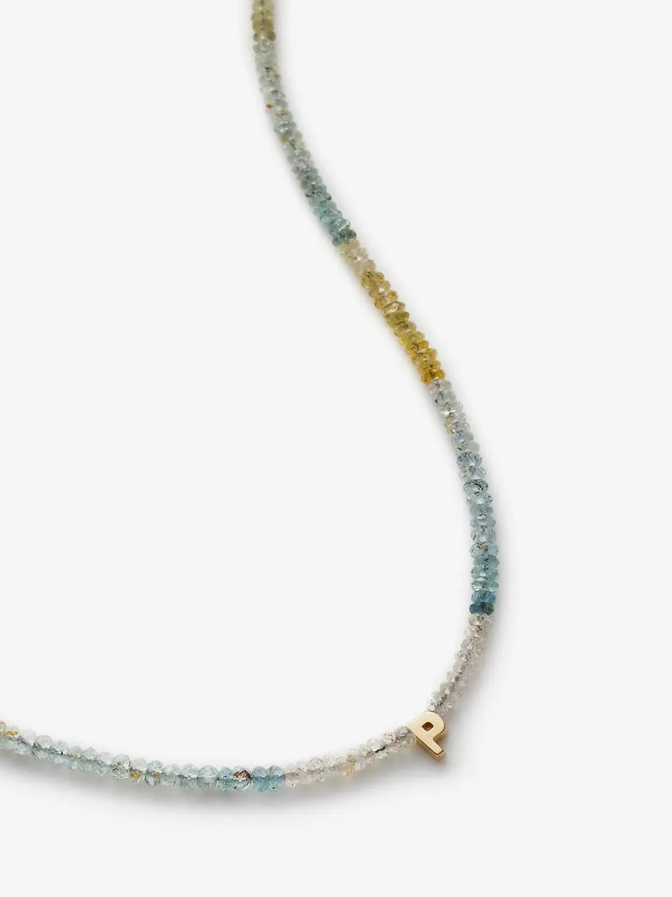 The One Letter Necklace in Aquamarine and 18k Gold is a delicate piece featuring small, multicolored beads in shades of blue, green, and yellow on an 18k gold chain. It boasts a single gold pendant shaped like the letter 'P' against a plain white background.