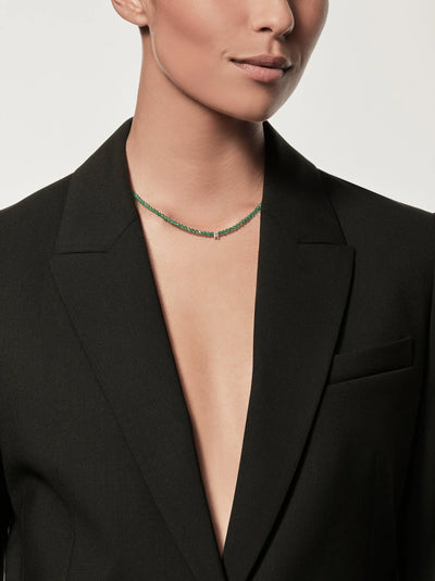 Cropped image of a person wearing a black blazer with no shirt underneath, showcasing the One Letter Necklace in Green Onyx and 18k Gold. The background is plain white.