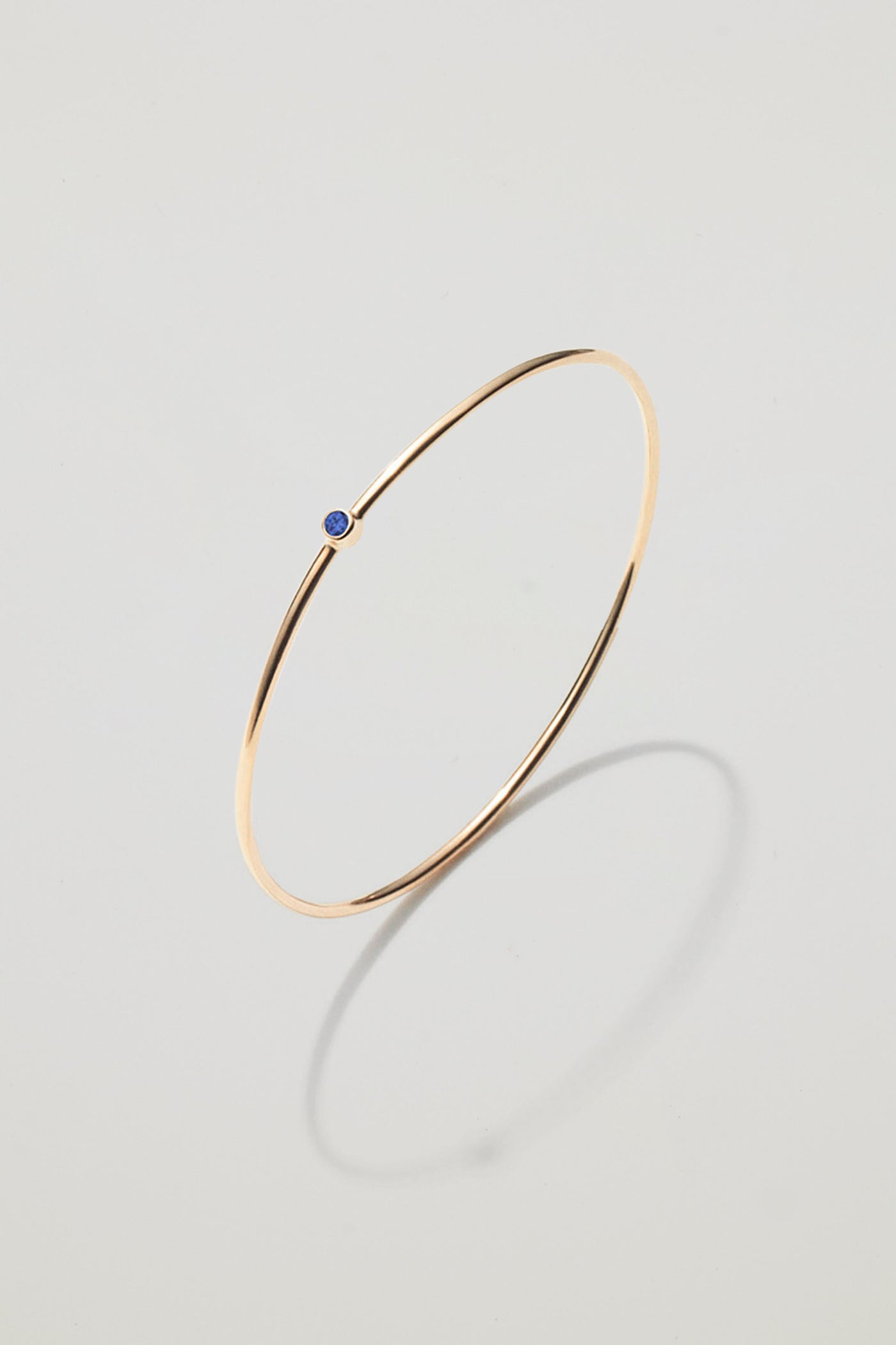 Solid gold bangle with a September sapphire birthstone, symbolising loyalty and wisdom.