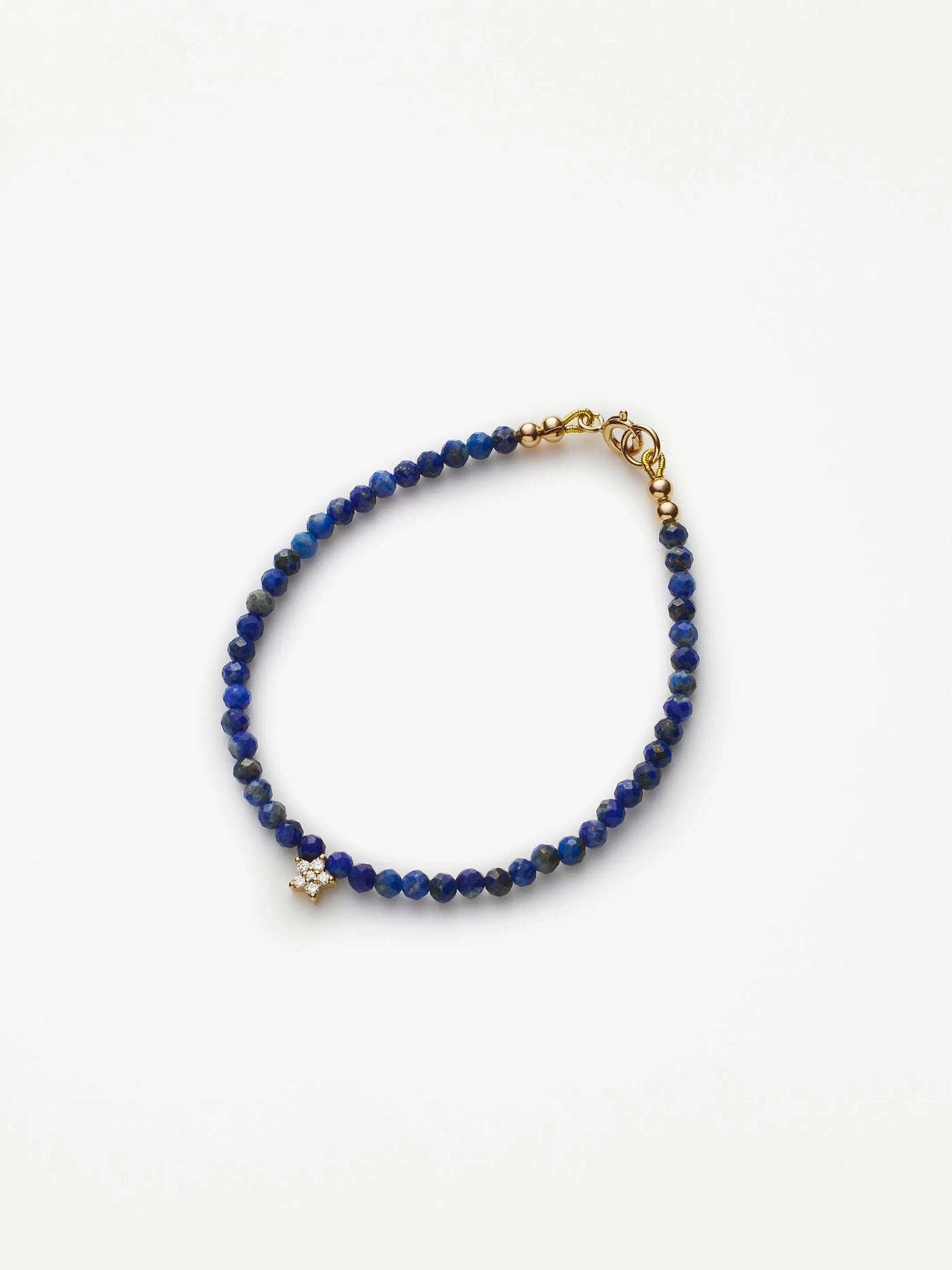 Introducing the Star Bracelet in Diamonds, Lapis Lazuli and 18k Gold: a beaded lapis lazuli bracelet adorned with small blue stones, featuring an 18k solid gold clasp and a sparkling diamond star charm. It boasts a simple yet elegant design, beautifully showcased against a plain white background.