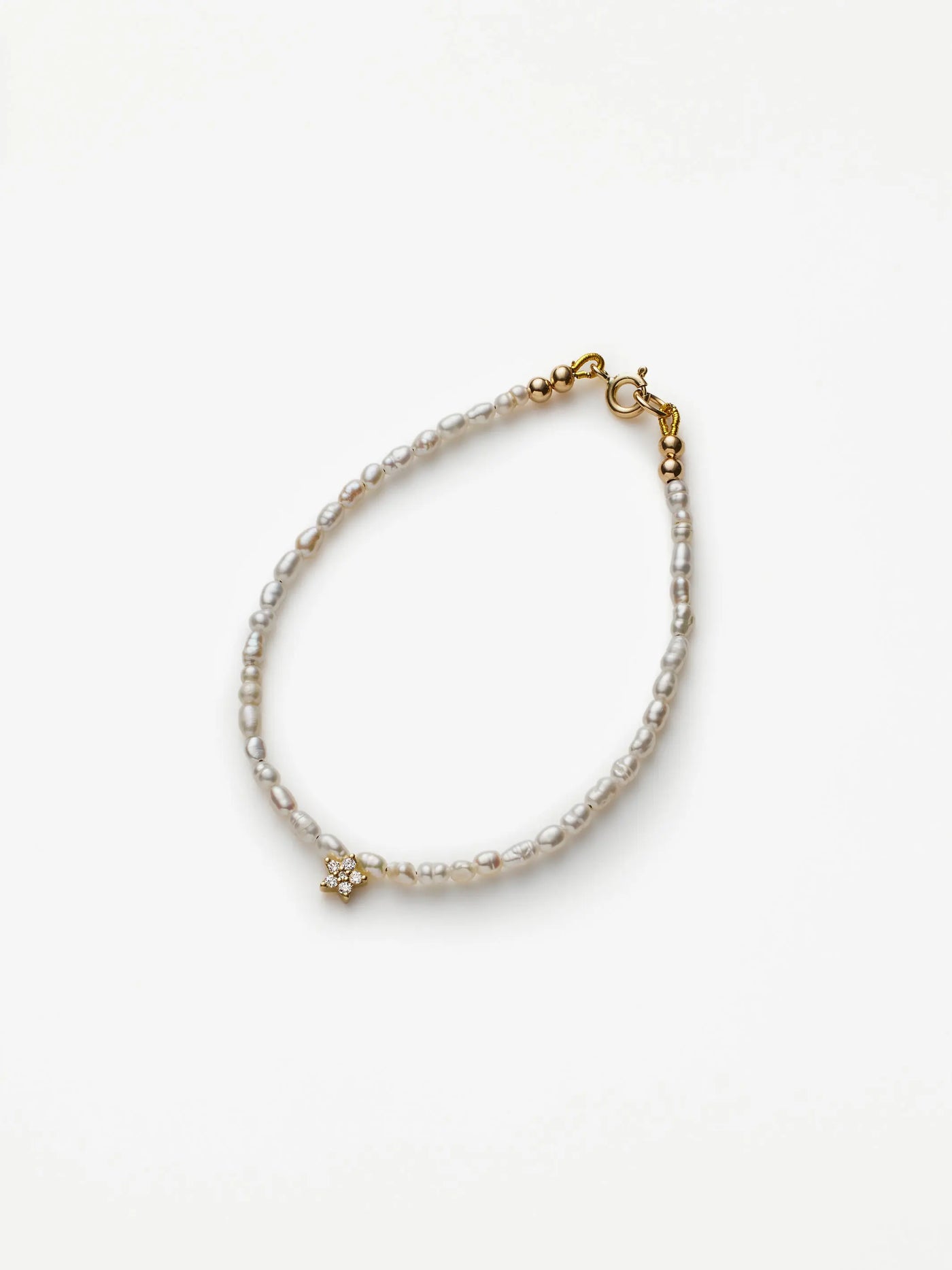 The Star Bracelet in Diamonds, Pearl, and 18k Gold is a delicate accessory featuring a strand of small, white freshwater pearls. It showcases a tiny gold flower charm adorned with a small pearl at its center. Crafted from 18k solid gold, this bracelet is secured with a small gold clasp, while the white background accentuates its elegance.