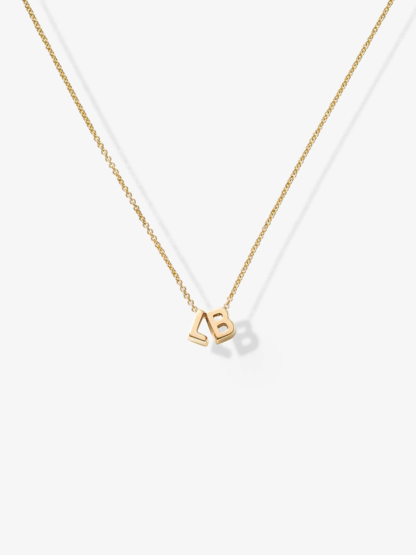 The Two Letters Necklace in 18k Gold showcases a delicate 18k solid gold chain with two gold letter charms, "L" and "B," elegantly positioned close together at the center, all set against a plain white background.