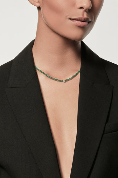 Cropped image of a person wearing a black blazer with no shirt underneath, showcasing the One Letter Necklace in Green Onyx and 9k Gold. The background is plain white.