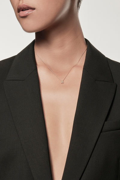 Close-up of a woman wearing a minimalist 18k gold initial “A” necklace on a fine chain, styled with a black blazer – personalised alphabet pendant jewellery