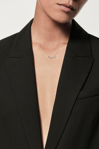 Close-up of a woman wearing a minimalist 18k gold and diamond initials “C” "A" "J" "C" necklace, styled with a black blazer, personalised alphabet pendant jewellery