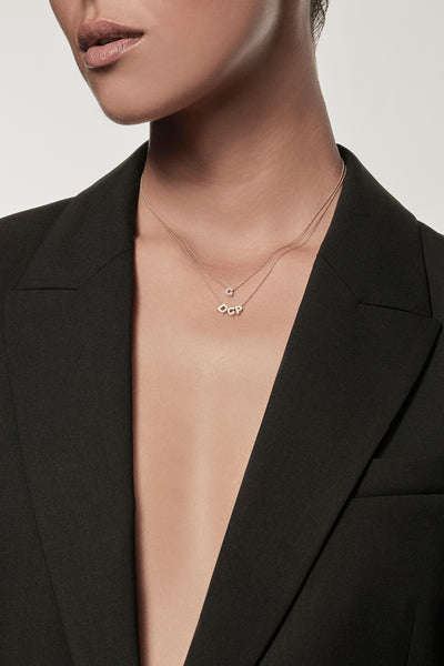 Close-up of a woman wearing a minimalist 18k gold initials “D" "C" "P" necklace and diamond "G" necklace on a fine chain, styled with a black blazer – personalised alphabet pendant jewellery