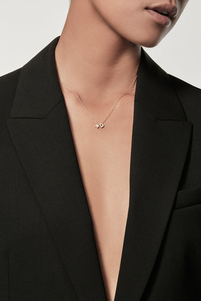 Close-up of a woman wearing a minimalist 18k gold initial “C” and gold star necklace on a fine chain, styled with a black blazer – personalised alphabet pendant jewellery