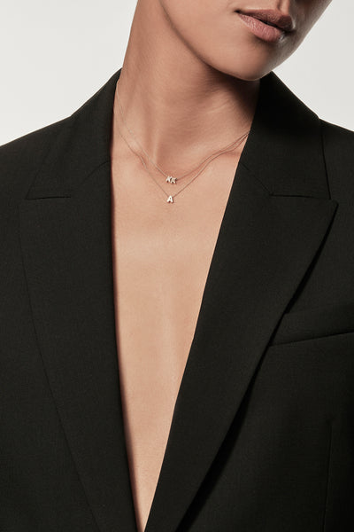 Close-up of a woman wearing a minimalist 18k gold initials “K” "K" necklace and lab-grown diamonds, styled with a black blazer – personalised alphabet pendant jewellery