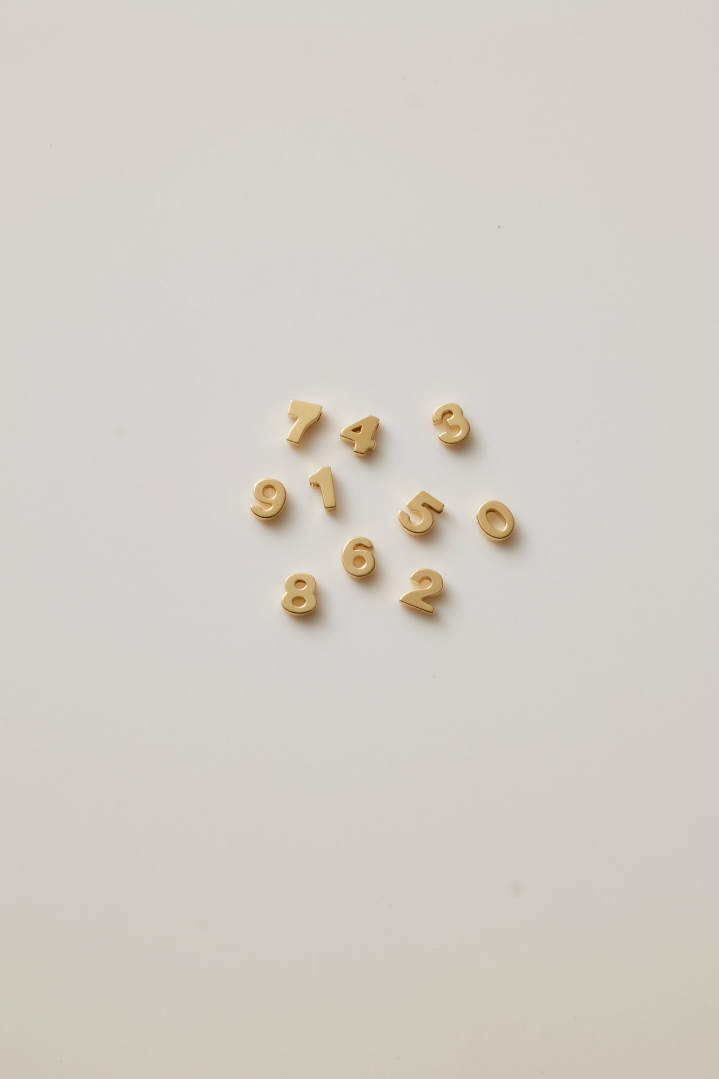 Small solid gold number charms (0-9), designed to slide onto a necklace chain for a personalised jewellery piece with symbolic meaning.