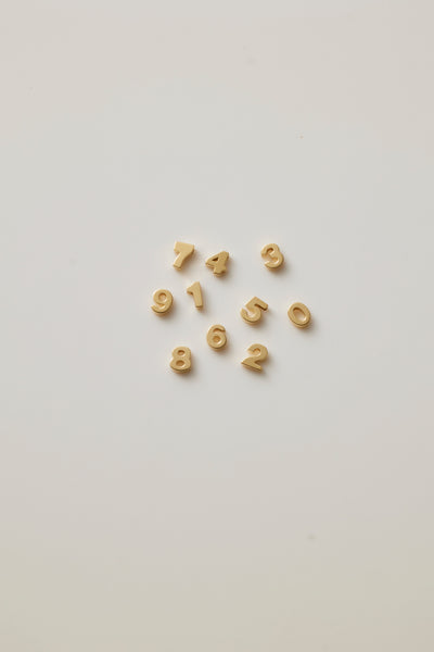Small solid gold number charms (0-9), designed to slide onto a necklace chain for a personalised jewellery piece with symbolic meaning.