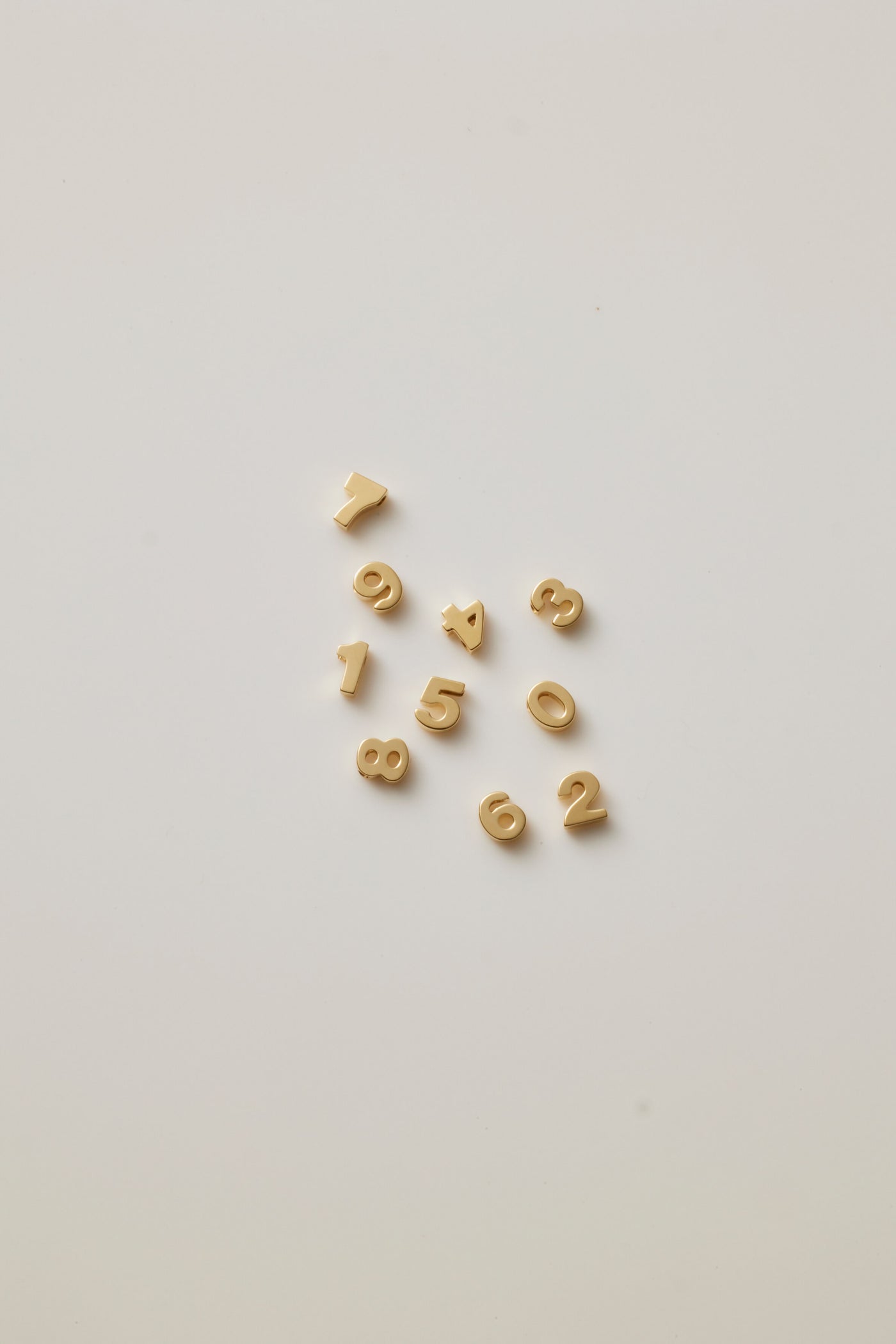 Small solid gold number charms (0-9), designed to slide onto a necklace chain for a personalised jewellery piece with symbolic meaning.