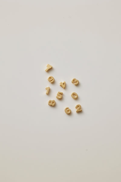 Small solid gold number charms (0-9), designed to slide onto a necklace chain for a personalised jewellery piece with symbolic meaning.